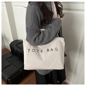 Detail of beige corduroy tote bag with black TOTE BAG embroidery text shown on model
