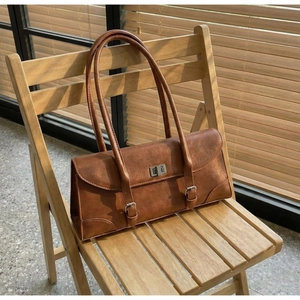Detail of vintage brown leather baguette bag with metal twist lock on a wooden chair