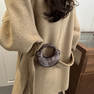 Sac croissant métallique avec texture ondulée et chaîne dorée sur un manteau camel
