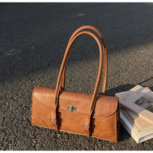 Close-up of a vintage brown leather underarm bag with silver twist lock on street background