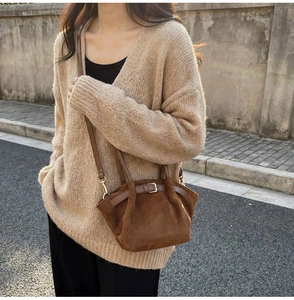 Close-up of brown suede shoulder bag with gold metal buckle and leather strap detail
