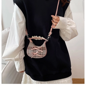 Detail of checkered crossbody bag with pink leather trim and decorative bows on model