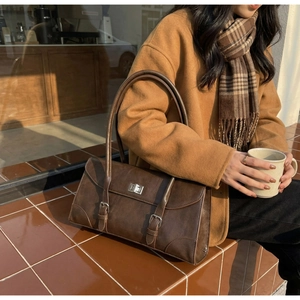 Detail of dark brown vintage leather shoulder bag with silver twist lock on camel coat background