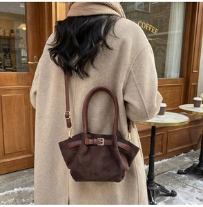 Close-up of a dark brown suede dumpling bag with a decorative leather buckle and strap