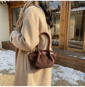 Detail of dark brown suede handbag featuring leather straps and decorative buckles