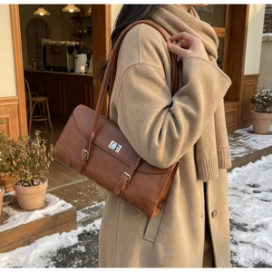 Detailed view of a vintage brown leather underarm bag with silver turn-lock and buckle strap