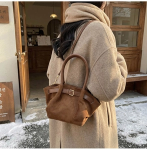 Detail of dark brown suede handbag with gold buckle on a beige wool coat background