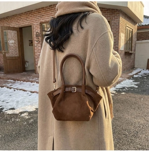 Macro detail of deep brown suede hobo bag with belt buckle decoration in a winter setting
