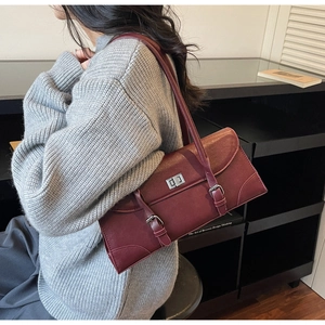 Detail of burgundy vintage baguette bag with silver buckle and straps on a grey sweater