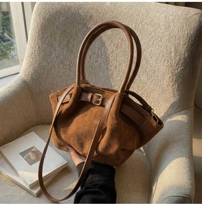 Close-up of brown suede handbag with ring handle and metal buckle on armchair