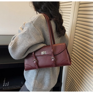 Detail of burgundy underarm bag featuring silver turn-lock and decorative straps on leather