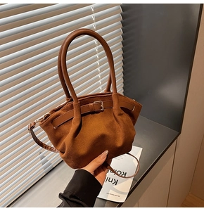 Detailed view of brown suede handbag featuring round handles and pleated texture finish