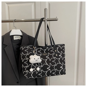 Detail of star-patterned black tote bag with long straps and white cloud plush charm
