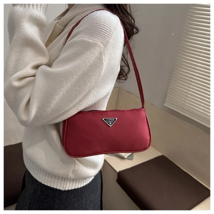Close-up of deep red nylon baguette bag with triangle metal logo plaque on a shoulder strap