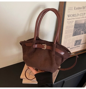 Detail of a dark brown suede handbag with decorative belt buckle and cylindrical handles