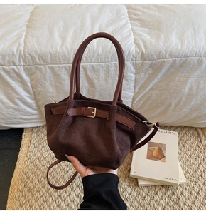 Close-up of a dark brown suede handbag with decorative belt buckles and natural pleats