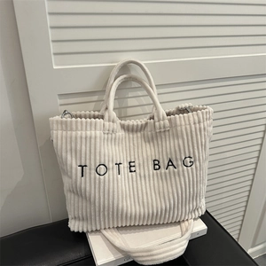 Cream corduroy tote bag with black embroidery and shoulder strap on white background