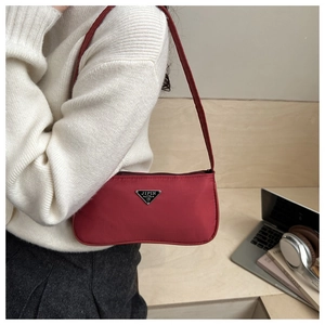 Detail of burgundy nylon underarm bag with metal logo, showing elegant lifestyle styling