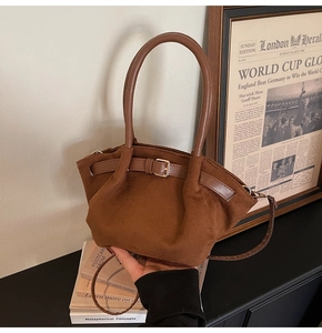 Close-up of brown suede tote bag with leather straps and metal hardware on vintage books