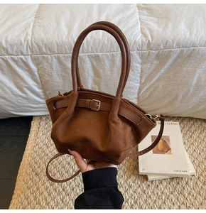 Detail of dark brown suede handbag featuring golden buckles and smooth leather handles