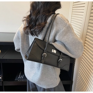 Back view of model wearing a black leather baguette underarm bag with silver hardware