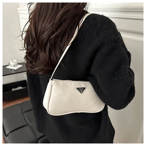 Close-up of minimalist beige shoulder bag with silver triangle plaque on a model
