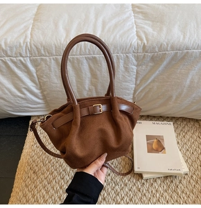 Close-up of brown suede bucket bag with gold buckle and leather handle on soft bedding