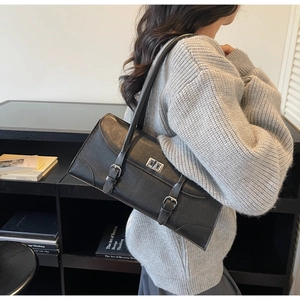 Detail of a black retro baguette underarm bag with silver buckles and a twist-lock closure