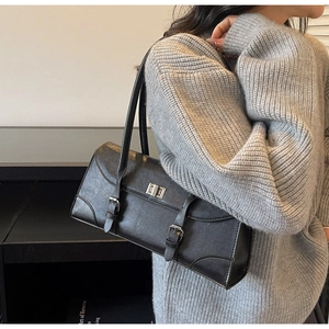 Detail of a minimalist black underarm bag with silver turn-lock and buckle strap detail