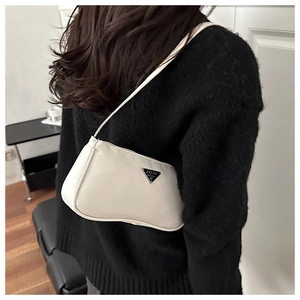 Detail of a creamy white faux leather baguette bag with a metal triangle logo on a model