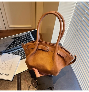 Detail of a brown suede handbag with natural pleats, dual handles, and a gold buckle strap