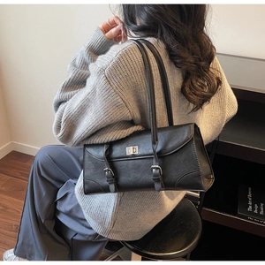 Detail of black leather baguette bag with silver twist lock on a shoulder strap