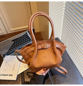 Close-up of brown suede handbag with unique round metal handle and strap detail