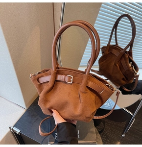 Close-up of brown suede handbag featuring pleated design and decorative leather buckle strap