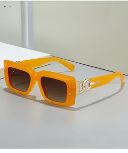 Detail of orange wide-frame sunglasses with bold gold metal chain link on temples