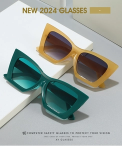 Macro shot of 2024 cat-eye sunglasses with green and amber frames on white geometric stand
