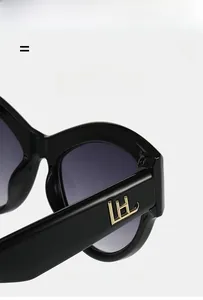 Detail of lightweight black cat-eye sunglasses with golden metal logo and grey lenses
