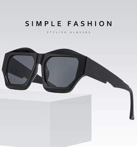 Detail of chunky black geometric sunglasses with thick frames and grey lenses on a stand