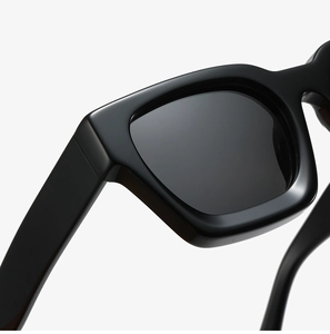 Close-up of sleek black thick-frame sunglasses showing glossy finish and hinge detail