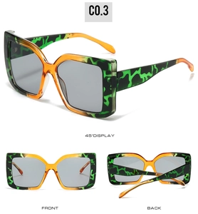 Detail view of large square sunglasses with orange and green camo texture and grey lenses