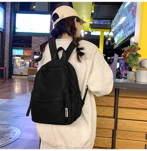 Rear view of a model wearing a black corduroy backpack with retro side label detail
