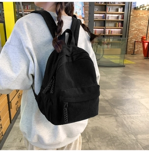 Side view of a black corduroy backpack with zipper pocket, shown worn in a bookstore