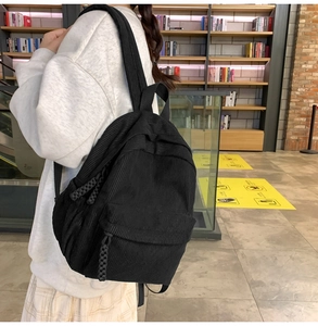 Detail of black corduroy backpack with woven zipper pulls in a library setting