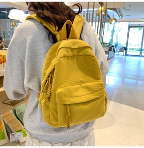 Detail of yellow corduroy backpack featuring a woven zipper pull and front pocket
