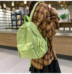 Detail of light green corduroy backpack with woven zipper pull and brand label