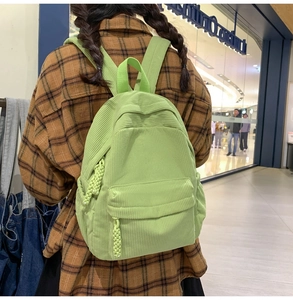 Close-up of a light green corduroy backpack with woven rope zipper detail in a mall