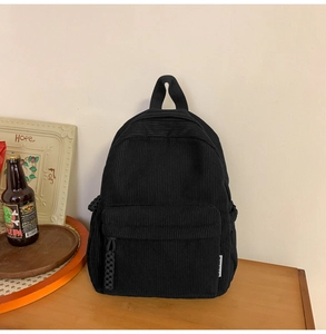 Detailed view of black corduroy backpack on a wooden desk with a vintage minimalist aesthetic