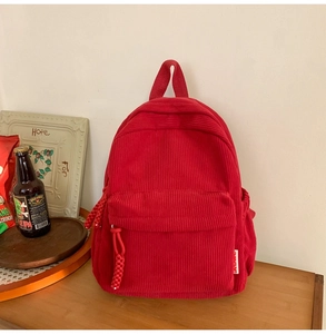 Detailed texture of red corduroy backpack with woven rope zipper on a vintage wooden desk