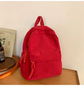 Close-up of red corduroy backpack with front zipper pocket and woven puller on wood table