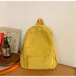 Close-up of yellow corduroy backpack showing fine texture, side pocket and side brand label